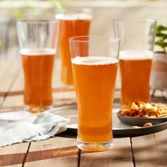 three glasses filled with beer sitting on top of a wooden table next to plates of food