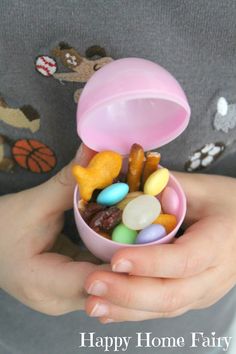 a person holding a pink bowl filled with candy and candies in it's hands