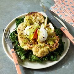 a white plate topped with cauliflower and an egg on top of it next to a fork