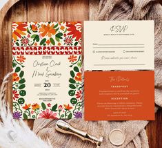 an orange and green floral wedding suite on top of a wooden table next to a feather