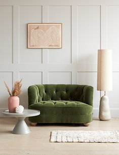 a living room with a green velvet couch and white rug on the wooden flooring