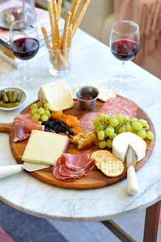 a wooden plate topped with cheese and meats next to two glasses of red wine