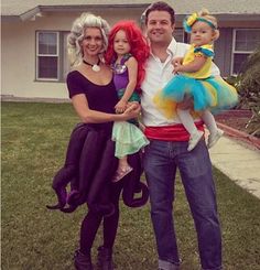 a man and two women standing in front of a house with their child on her lap