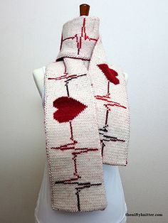 a white scarf with red designs on it sitting on top of a mannequin