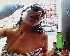 a woman in a bathing suit holding a green bottle and pointing at the camera with her tongue out