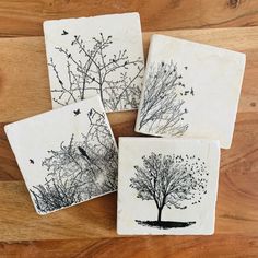 four coasters with black and white trees on them sitting on a wooden table top