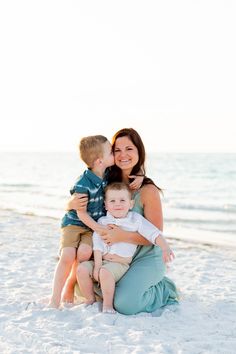 a mother and her two sons on the beach in front of the ocean at sunset