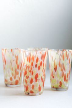 four glass cups sitting next to each other on a white counter top in front of a wall