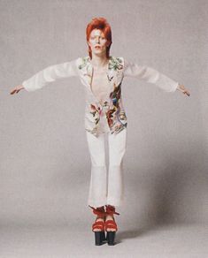 a woman with red hair and white pants is standing in front of a gray background