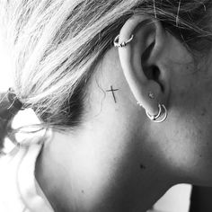 a woman's ear has a cross tattoo on it, while the rest of her ear is in black and white