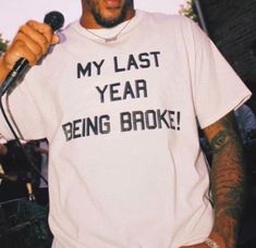 a man holding a microphone and wearing a t - shirt that says my last year being broke