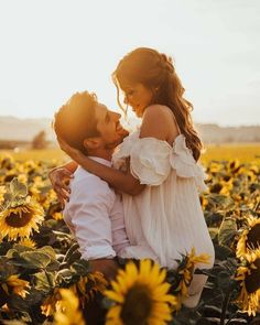 a man and woman are hugging in the middle of a field of sunflowers