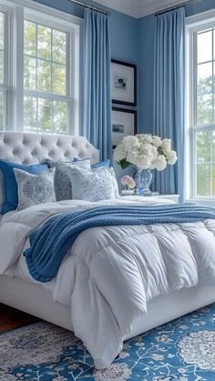 a bedroom with blue walls and white bedding, windows, and rugs on the floor