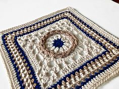 there is a crocheted square on the table with a blue and white design