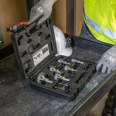 a man in safety gear holding a tool box with tools inside it on a table