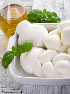 mozzarella and olive oil are being poured into a white dish on a wooden table