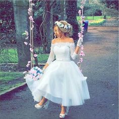 a woman in a white dress is swinging on a swing with pink flowers around her