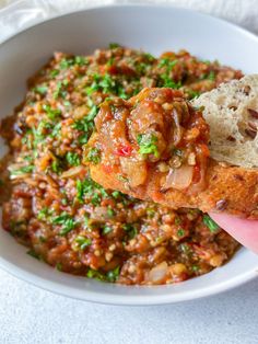 a hand holding up a piece of bread over a bowl of beans and meat stew