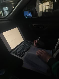 a person sitting in a car with a laptop computer on their lap and writing notes