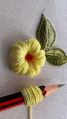 two crocheted flowers are next to a pencil