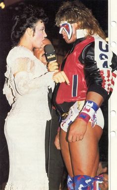 a man and woman in wrestling gear talking to each other on the stage with microphones