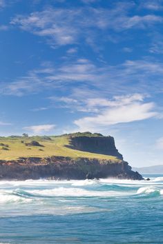 an ocean view with waves crashing on the shore and a large cliff in the background