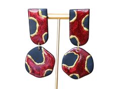 Elevate your style with these bold and sophisticated earrings! Featuring a striking red  and black pattern with gorgeous gold accents, these polymer clay dangles bring a touch of luxe to any outfit. Inspired by organic shapes and artistic flair, these statement earrings are both elegant and modern--perfect for those who want to stand out. Each pair is handcrafted with care, giving every earring a one-of-a-kind charm that reflects the beauty of imperfections. Whether you're dressing up for a special occasion or adding a pop of style to your everyday look, these earrings are sure to turn heads. Handmade with polymer clay Red and black design with hand-painted gold accents Lightweight and comfortable for all-day wear Hypoallergenic earring hooks Note: Due to the handmade nature of these earri Red Hand Painted Polymer Clay Earrings, Hand Painted Red Polymer Clay Earrings, Red Drop Earrings In Polymer Clay, Hand Painted Red Elegant Earrings, Elegant Hand Painted Red Earrings, Elegant Red Polymer Clay Earrings, Red Polymer Clay Earrings, Sophisticated Earrings, Black Statement Earrings