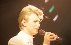 a man holding a microphone in his right hand and wearing a white suit on stage