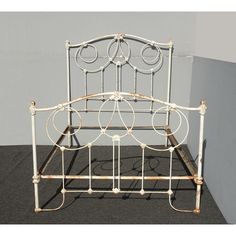 an old iron bed frame with white paint on the top and bottom rails, in front of a gray wall