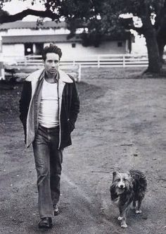 a black and white photo of a man walking next to a dog on a dirt road