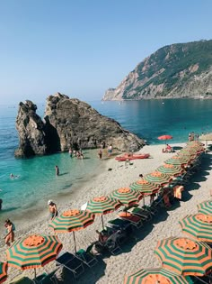 many umbrellas are set up on the beach with people swimming and sunbathing