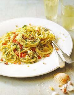 a white plate topped with pasta and vegetables next to a glass of water on top of a table