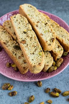 several pieces of bread on a pink plate with pistachios around the edges