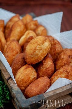 a wooden box filled with fried donuts on top of a green tablecloth next to a pile of pine needles