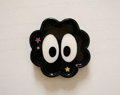 a black plate with eyes and stars in the center on a white wall behind it