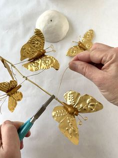 someone is cutting out some gold butterflies from the top of a piece of metal wire