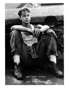 a black and white photo of a young man sitting on the ground with his legs crossed