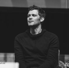 a black and white photo of a man sitting in a chair looking off to the side