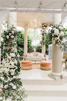 an outdoor wedding venue with white flowers and greenery on the columns, couches and chandelier