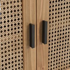 two black handles on a wooden cabinet with perforated screen in the back ground