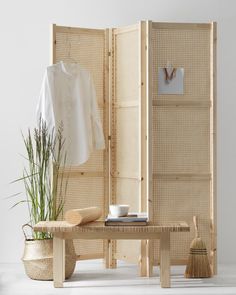 a room divider made out of bamboo with a plant in the corner and a white shirt hanging on it