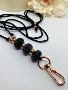 a black and gold beaded key chain on a white table next to a flower