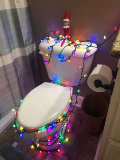 an elf is sitting on top of a toilet in the bathroom decorated with christmas lights