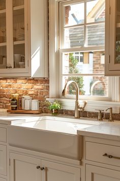 a kitchen with white cabinets and a brick wall behind the sink is seen in this image