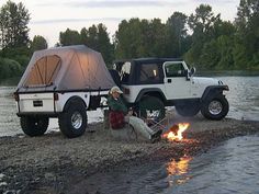 a man sitting in front of a campfire next to a white truck with a tent on it