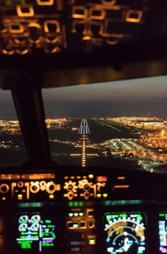 the view from inside an airplane at night, looking down on a runway and lights in the distance