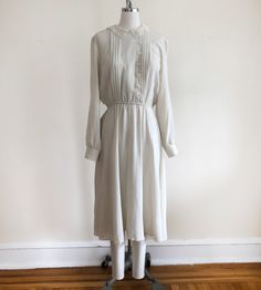 "Long-sleeved, ivory dress with pintucks and embroidered lace collar, from the 1980s. Bust measures 19\" (48.5 cm) flat across and waist measures 12-17.5\" (30.5-44.5 cm) flat across. The dress is 45\" (114 cm) in length. Original size is an 11. Cotton blend." Cream Long Sleeve Midi Dress With Lace Trim, Fall Dresses With Lace Collar For Daywear, Cream Long Sleeve Dress With Lace Collar, Classic Long Sleeve Dress With Lace Collar, Classic Vintage Dress With Ruffles For Spring, Classic Victorian Dress With Lace Trim For Spring, Classic Cream Dress With Lace Trim, Classic Cream Dresses With Lace Trim, Classic Vintage Dress For Spring Formal