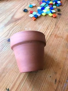 a clay pot sitting on top of a wooden table next to colorful beads and scissors