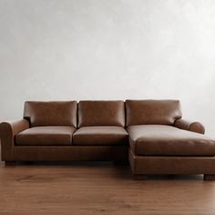 a brown leather couch sitting on top of a wooden floor next to a white wall