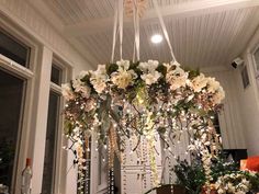 a chandelier with flowers hanging from it's ceiling in front of a window